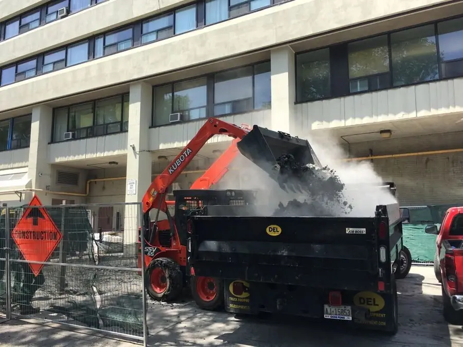 Skid steer loading demolition debris into a dump truck outside an apartment building