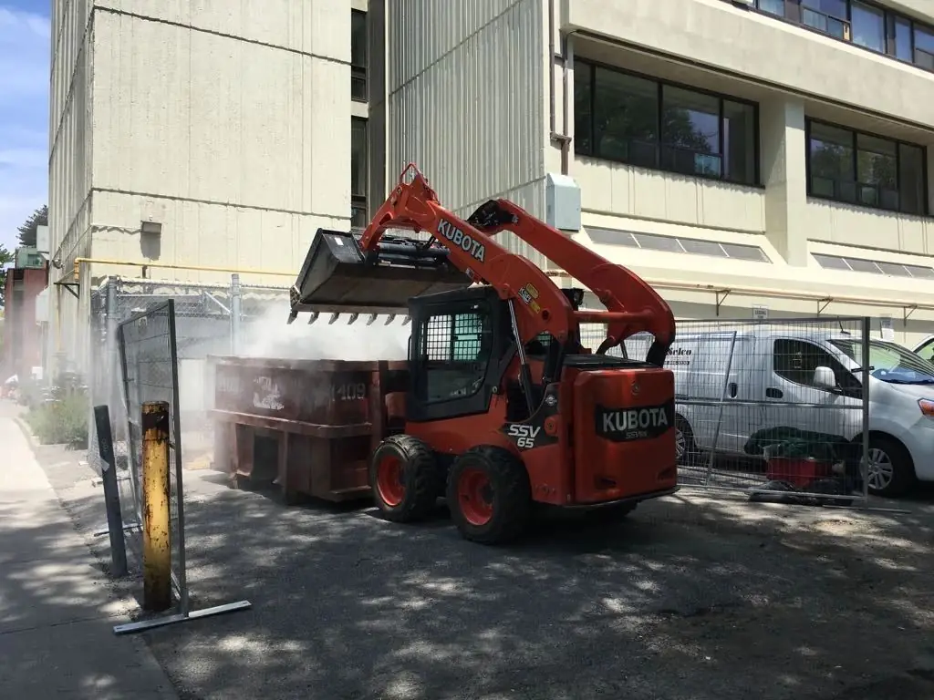 Skid steer unloading debris into a bin